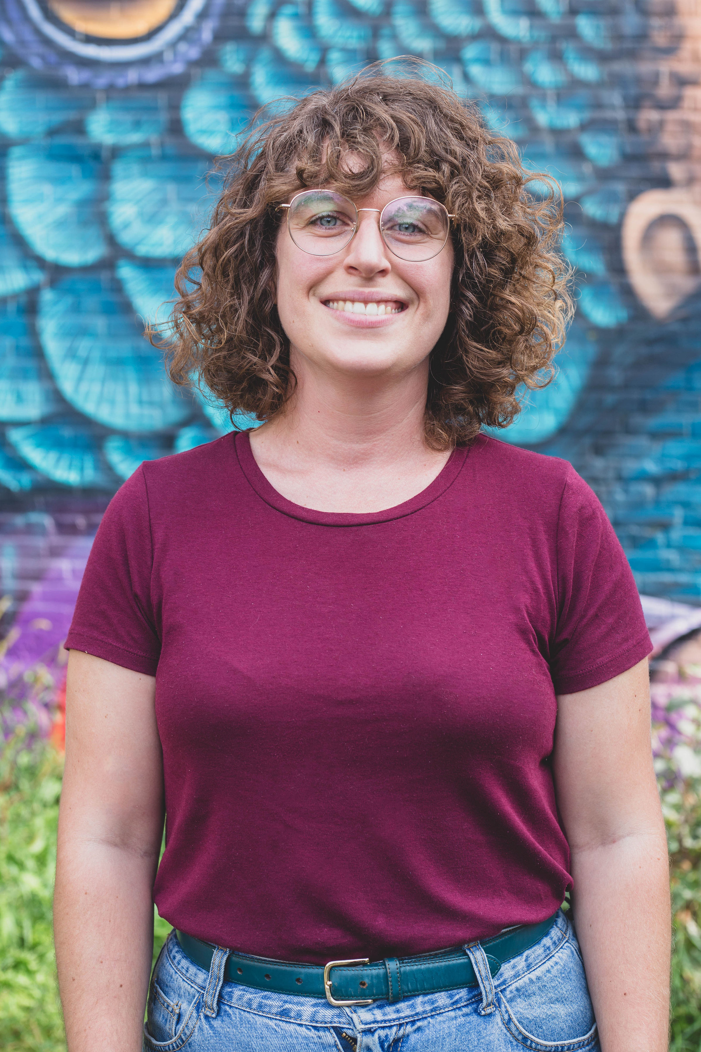 Marie-Eve a les cheveux mi-longs châtains. Elle porte des lunettes et un chandail bourgogne.